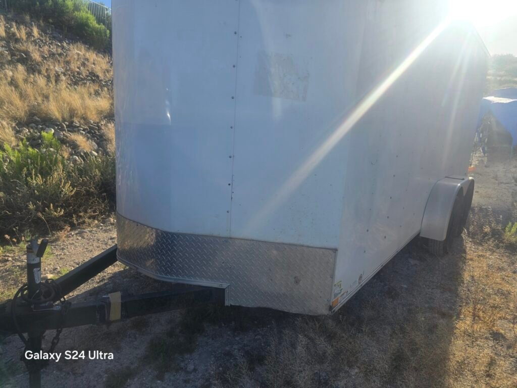 White enclosed cargo trailer with diamond plate front parked outdoors.