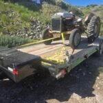 Old tractor secured on a Monsoon Trailer Rental LLC flatbed trailer.