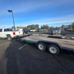 White pickup truck hitched to a flatbed trailer, with "MONSOON TRAILER RENTAL" text.