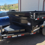 Black Ironbull dump trailer with a blue car and garage in background.
