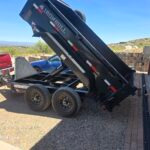 Black IronBull dump trailer tilted up, parked next to a red truck.